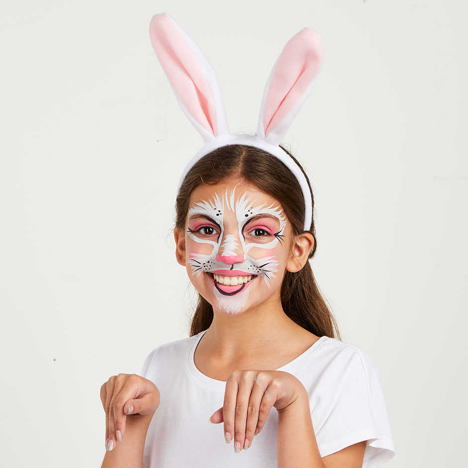 Child smiling with whimsical bunny face paint including pink ears and white whiskers at a spring festival.