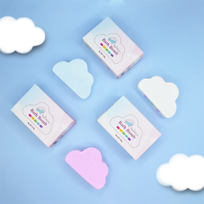 A child's hand holding a rainbow-colored Kids Bath Bomb above a tub filled with bubbles.